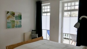 A bedroom with a large bed, a chair, a radiator, and a window with curtains. - Holiday Apartment Palais am Park (Kuehlungsborn)