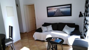 A living room with a sofa, a coffee table, and a TV. There is a door leading to another room and a window with curtains. - Holiday Apartment Palais am Park (Kuehlungsborn)