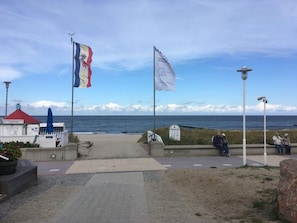 A coastal walkway with flags, a red-roofed building, and a view of the sea.
