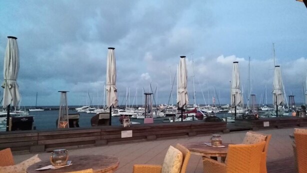 An outdoor seating area with wicker chairs and tables, overlooking a marina with numerous sailboats. - Holiday Apartment Palais am Park (Kuehlungsborn)