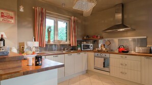 A modern kitchen with white cabinets, a stainless steel range hood, a microwave, and a toaster. There is a window with curtains, a sink, and a countertop with various kitchen items. - Luxury Holiday Home With Private Garden (Waimes)