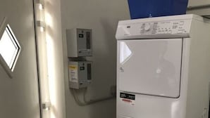 Une buanderie avec des machines à laver et des sèche-linge superposés, un panier à linge bleu posé sur le dessus, et une porte avec une fenêtre.
