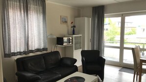 Un salon comprenant un canapé en cuir noir, une table basse blanche, un fauteuil noir et un meuble blanc contenant un four à micro-ondes.