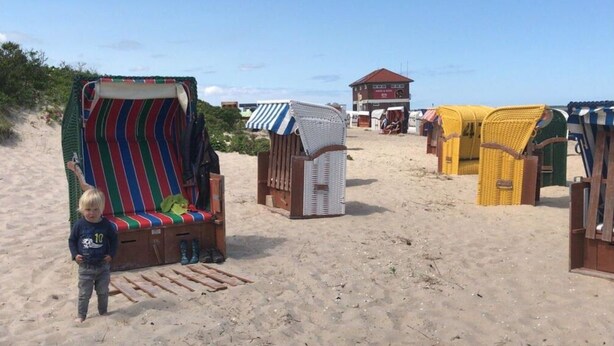 Une plage de sable avec des chaises de plage colorées et un petit bâtiment en arrière-plan.