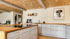 A modern kitchen with a wooden ceiling, white cabinets, and a central island with a black induction cooktop. - 5 Star Holiday Home in Laeso-by Traum (Læsø)