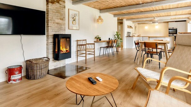 A spacious living area with a fireplace, wooden flooring, and a modern kitchen in the background. - 5 Star Holiday Home in Laeso-by Traum (Læsø)