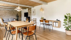 A modern dining area with a wooden table and chairs, a brick wall, and a television. - 5 Star Holiday Home in Laeso-by Traum (Læsø)