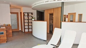 A reception area with a wooden reception desk, a shelf with folded towels, and two white lounge chairs. - Tasteful Apartment in Elzach-yach (Elzach)