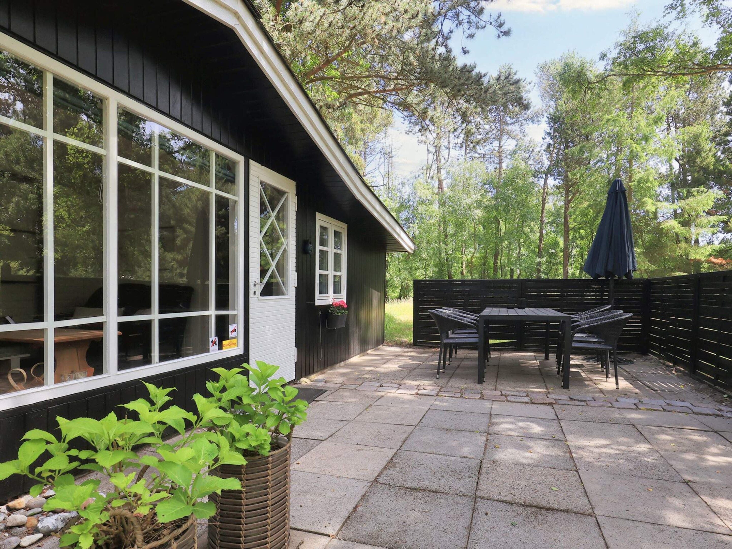 A patio with a table and chairs, a black fence, and a window with a view of trees.