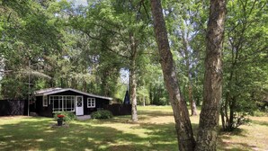 Une petite maison de plain-pied avec un porche à l’avant, entourée d’une pelouse et d’arbres.
