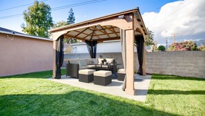 Un patio couvert aménagé avec du mobilier d’extérieur, une pergola et une pelouse bien entretenue.