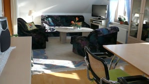 A living room with a sofa, a coffee table, a TV, and a dining table. - Ostenberg - Near CJD Comfortable Holiday Residence (Garz/Rügen)
