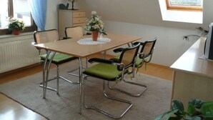 A dining area with a table, chairs, a radiator, a window with blue curtains, a plant, and a lamp. - Ostenberg - Near CJD Comfortable Holiday Residence (Garz/Rügen)