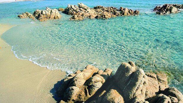 Una playa con agua turquesa cristalina, formaciones rocosas y una orilla arenosa.