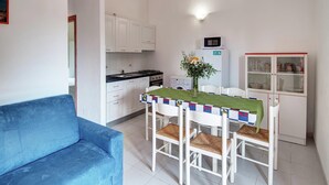 Cocina compacta con armarios blancos, una mesa de comedor con mantel verde y un sofá azul.