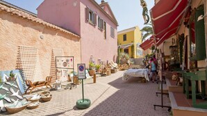 Una calle estrecha bordeada de tiendas, un cartel de 'no estacionar' y varios artículos a la venta.