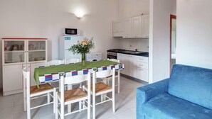 Una cocina compacta con armarios blancos, una mesa de comedor con mantel verde y un sofá azul.
