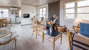 A cozy living room with wooden floors, a fireplace, and a television. There is a dining area with a table and chairs. - 6 Person Holiday Home in Henne (Henne)