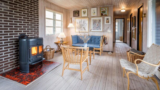 A cozy interior with a wood-burning stove, a blue sofa, wicker chairs, and framed artwork on the walls. - 6 Person Holiday Home in Henne (Henne)