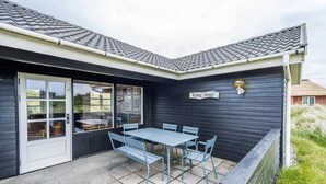 A black building with a tiled roof, a sign reading "Lyng huset," and a patio with a table and chairs. - 6 Person Holiday Home in Henne (Henne)
