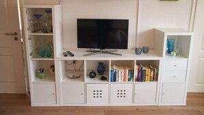 Una sala de estar con un televisor de pantalla plana, estanterías y un pequeño estante con objetos decorativos.