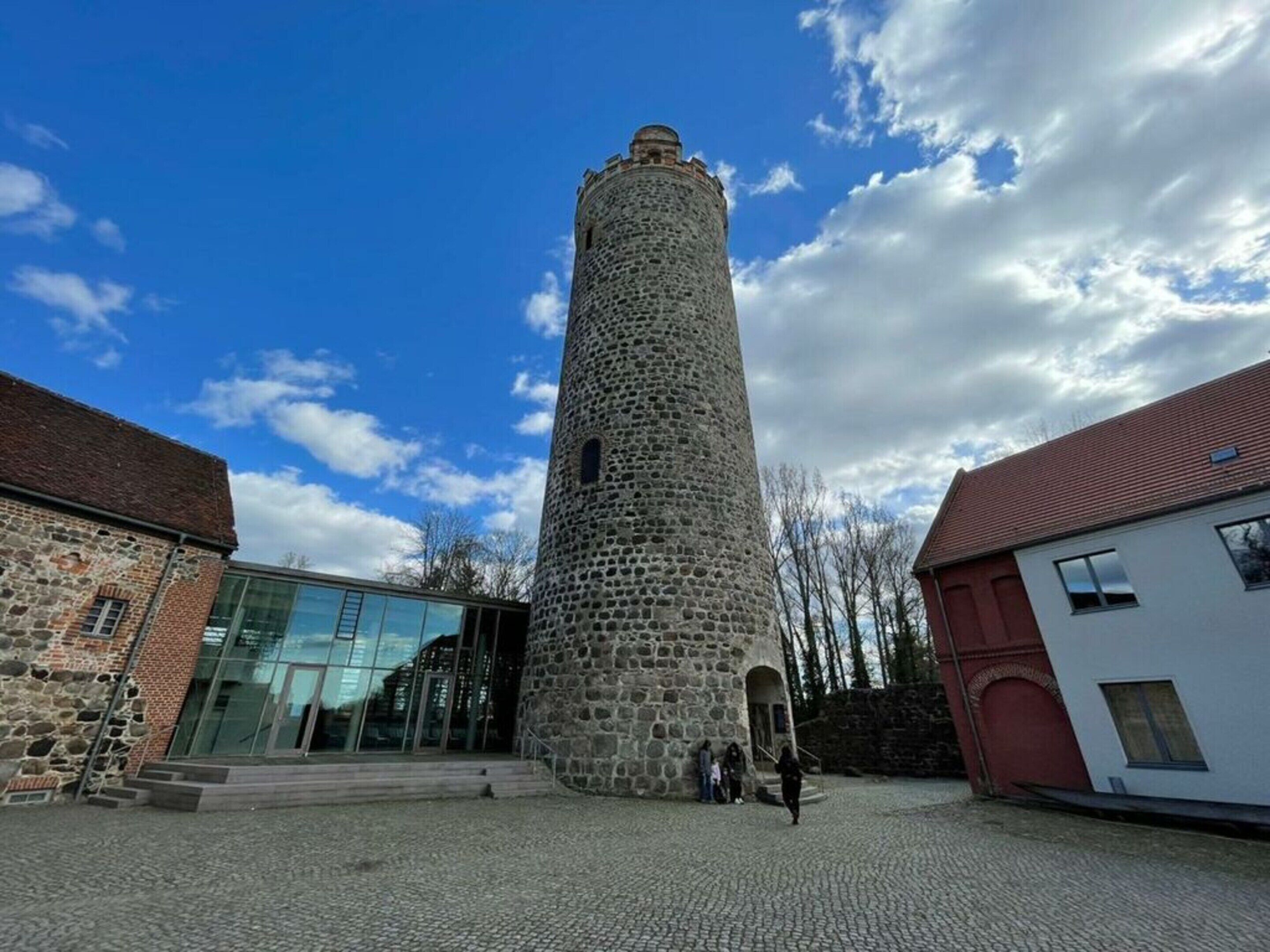 Ein steinerner Turm mit kreisförmigem Fundament und einer Kuppel, umgeben von Gebäuden mit moderner und traditioneller Architektur.