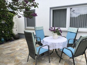 A patio with four wicker chairs and a table, surrounded by stone tiles and a white wall.