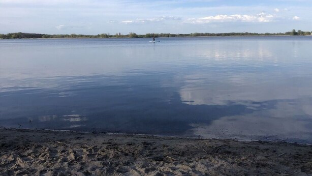 Un lago tranquilo con orilla arenosa y una costa lejana.