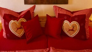 Una habitación con un cuadro grande de cabeza de ciervo en la pared, un sofá rojo a cuadros con almohadas con forma de corazón, y un cabecero de madera.