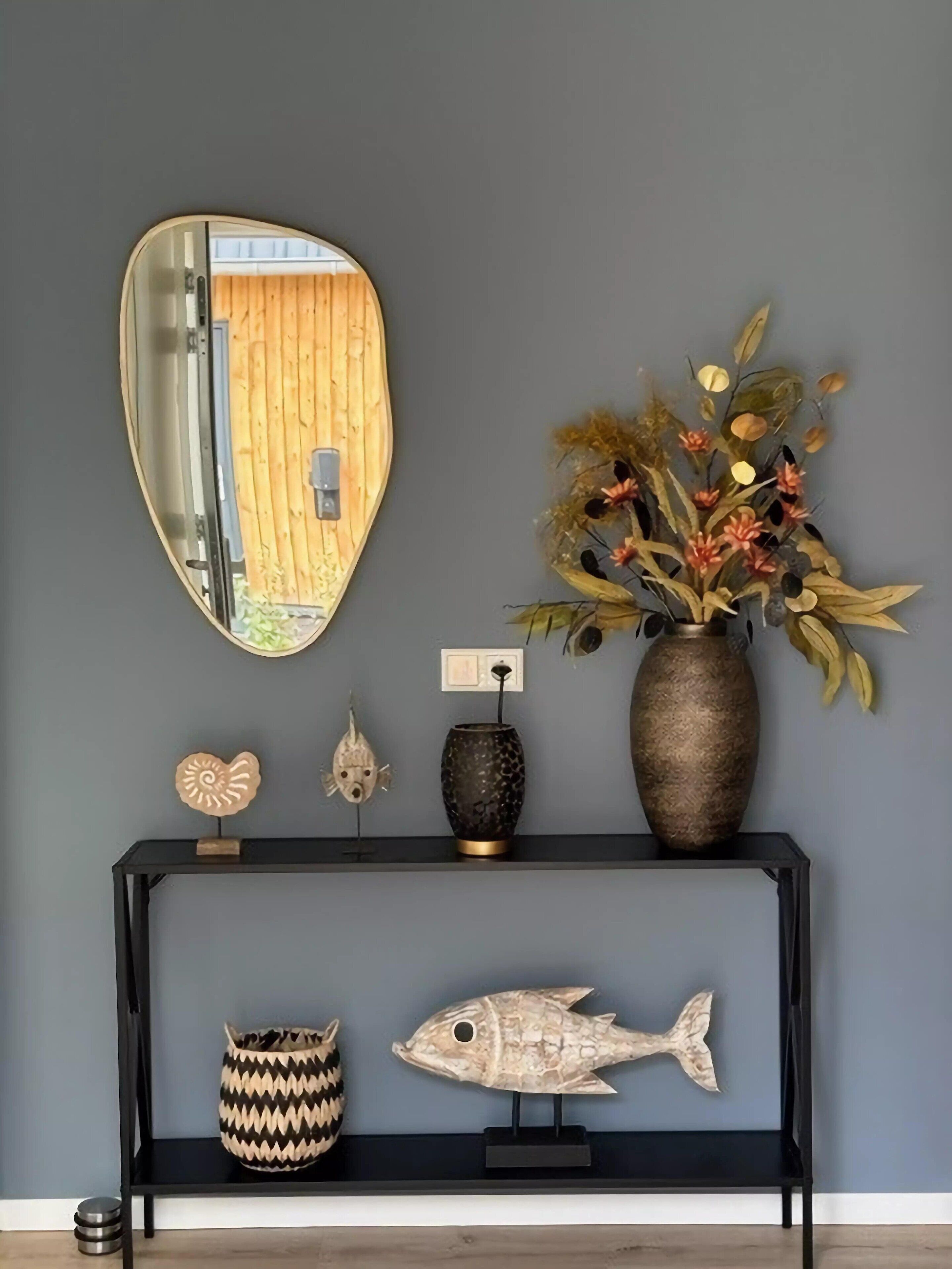 A wall with a mirror, a vase with dried flowers, and decorative fish and shells on a black console.