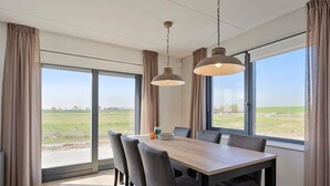 A modern dining room with a large table and chairs, large windows with curtains, and hanging pendant lights.