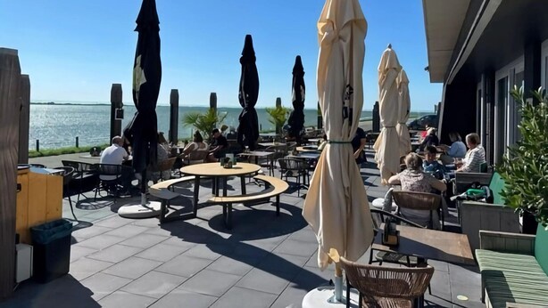 An outdoor patio with round tables and chairs, umbrellas, and a view of the sea.