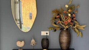 A wall with a mirror, a vase with dried flowers, and two decorative fish figures on a black console table.