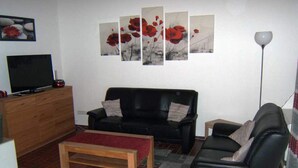 A living room with a black leather sofa, a wooden coffee table, a TV on a wooden cabinet, and a red rug.