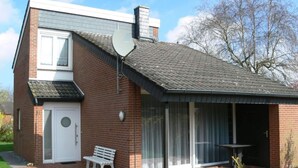 A two-story brick house with a covered patio area, a bench, and a satellite dish.