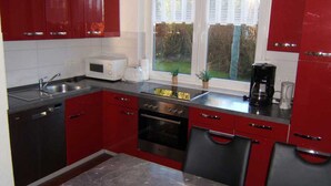 A compact kitchen with red cabinets, a built-in oven, a microwave, and a coffee maker.