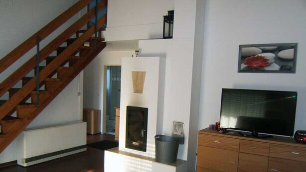 A modern living room with a wooden staircase, a fireplace, a television, and a red rug.