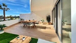 A modern outdoor patio with a wooden table and chairs, surrounded by potted plants and a small grassy area. - Sunny Escape in Playa Motril (Motril)