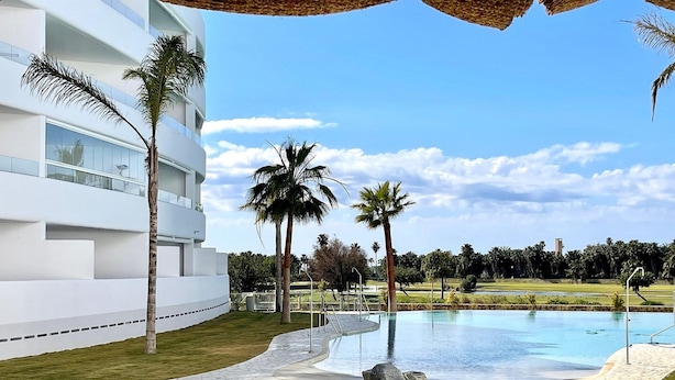 A modern hotel with a swimming pool, palm trees, and a clear blue sky. - Sunny Escape in Playa Motril (Motril)
