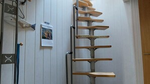 Un escalier en colimaçon avec des marches en bois et des rampes en métal, menant à l’étage supérieur.