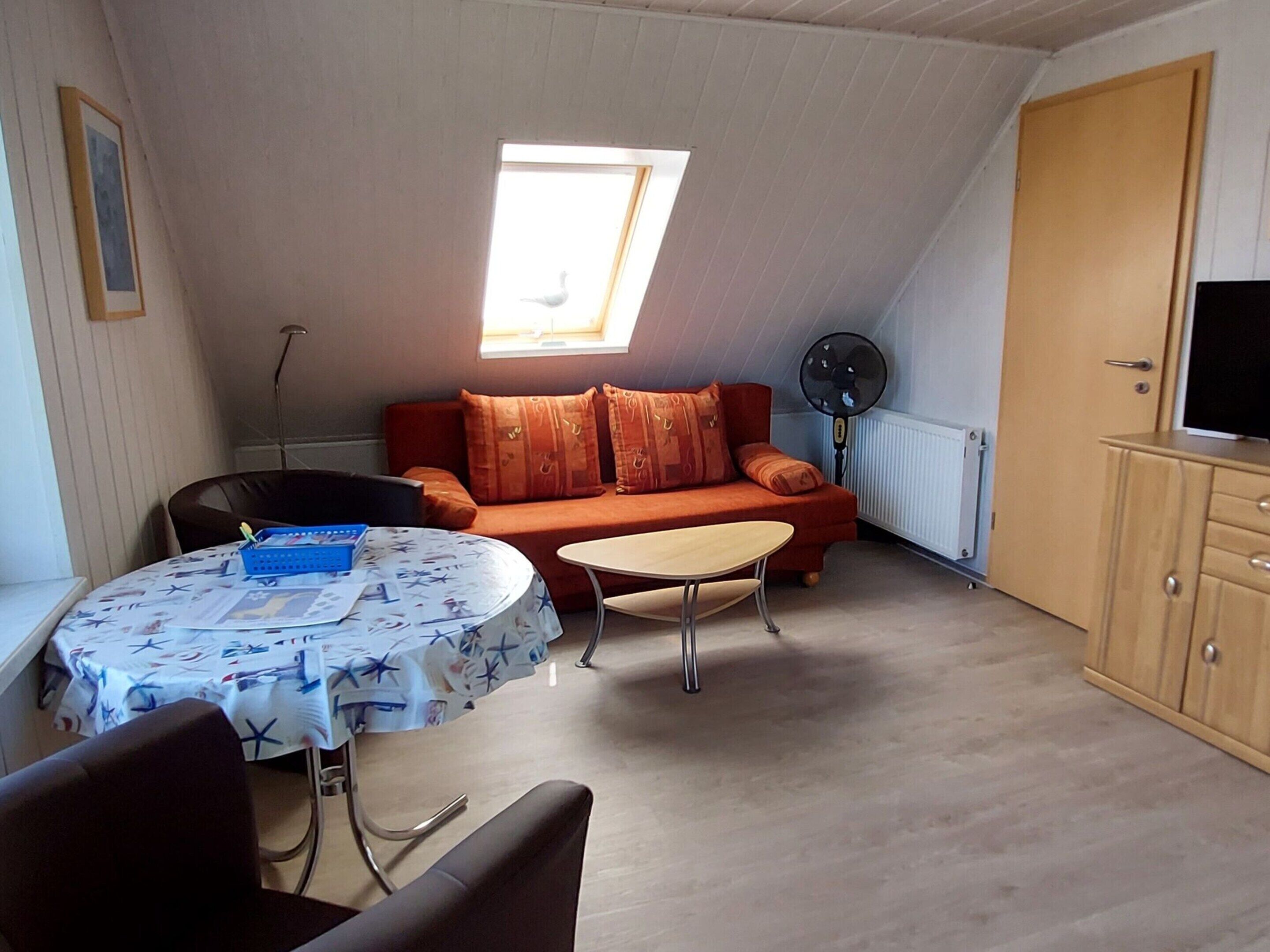 Ein gemütliches Dachzimmer mit einer Couch, einem Tisch, einem Fernseher und einem Fenster.