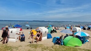 Une plage avec des tentes et des parasols, des gens dans l’eau et un ciel dégagé.