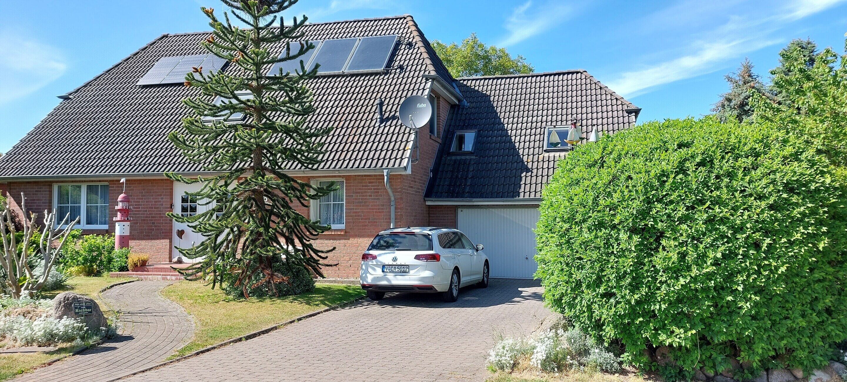 Et hus med bil på indkørslen, solpaneler på taget og en velplejet have.