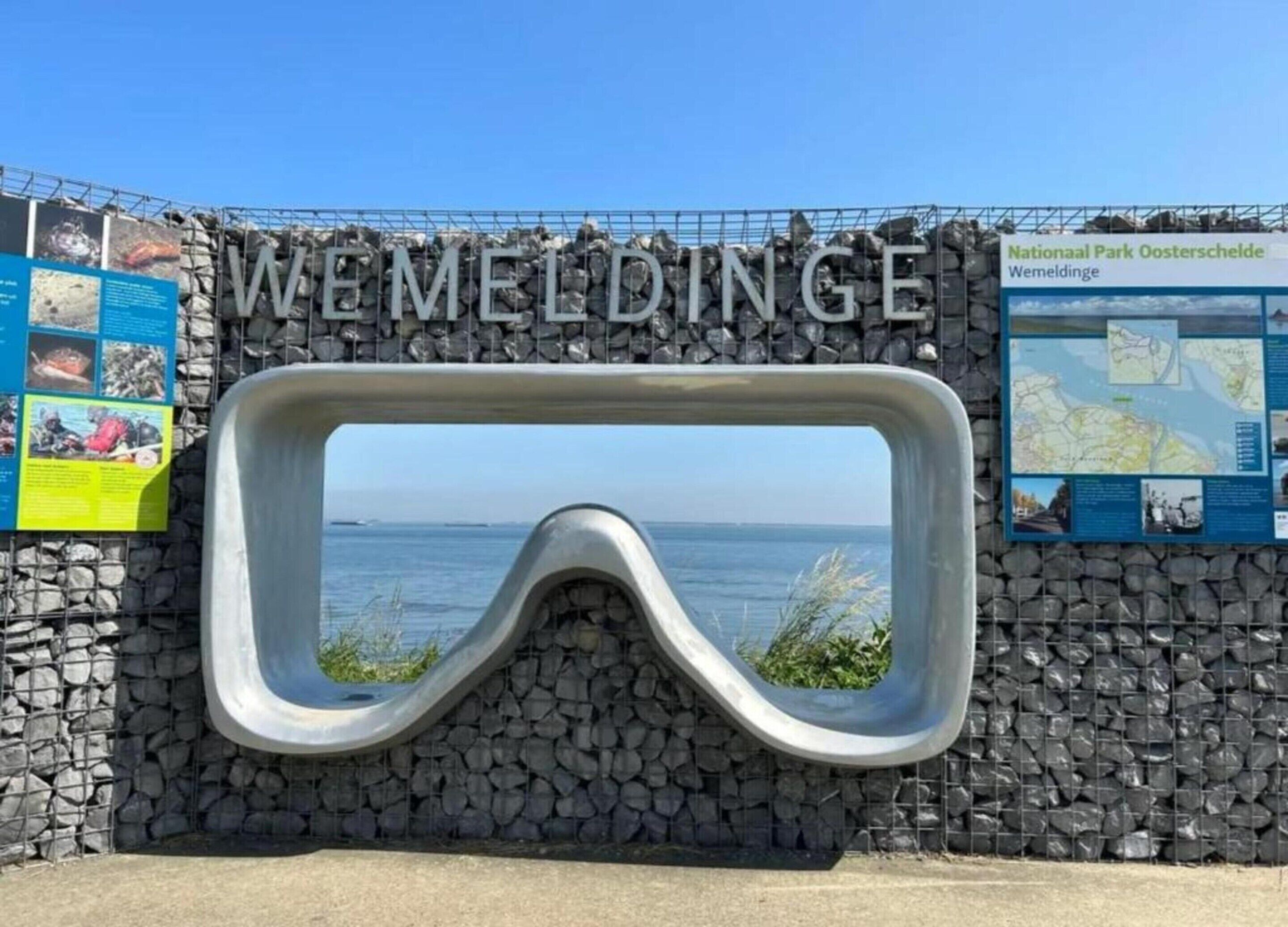 A diving board with the text "WEMELDINGE" above it, a stone wall, and a signboard with information.