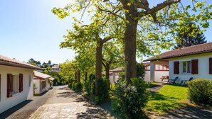 A narrow cobblestone street lined with white buildings with red shutters, leading to a covered patio area.