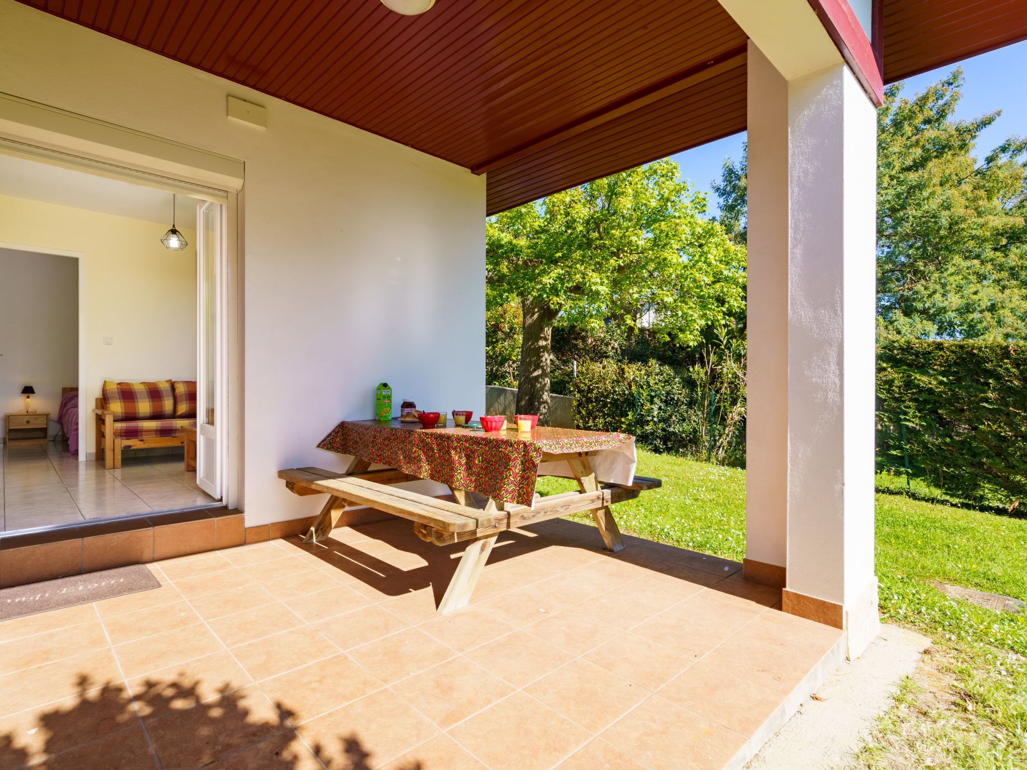 Un patio cubierto con una mesa lista para comer, un sofá y una puerta que da a un espacio interior.