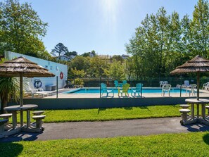 Relax by the pool surrounded by lush greenery and trees, with lounge chairs and tables for a serene escape.