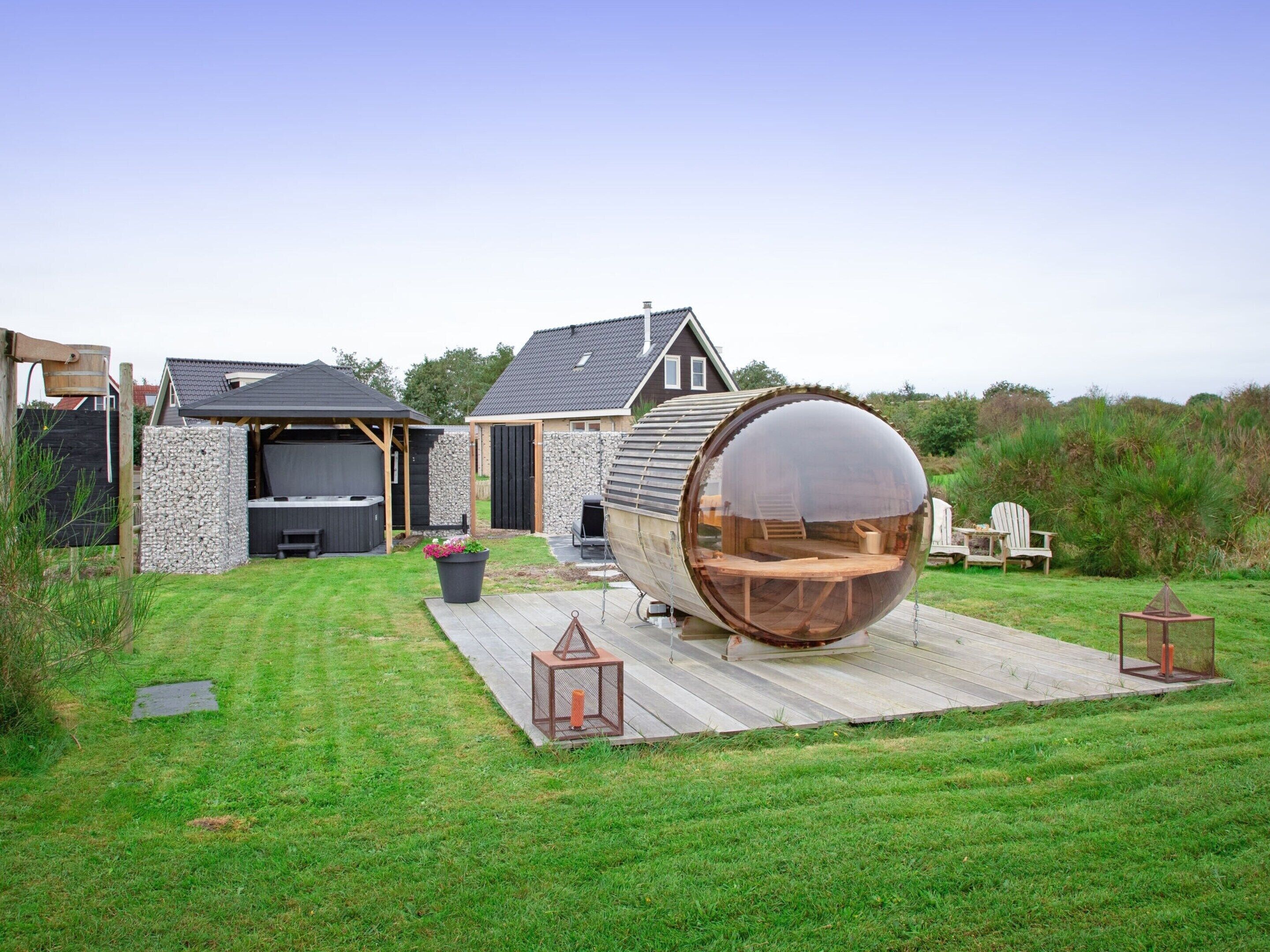 Een huis met een grote houten vatstructuur in de achtertuin, een jacuzzi en een terras met tuinmeubilair.