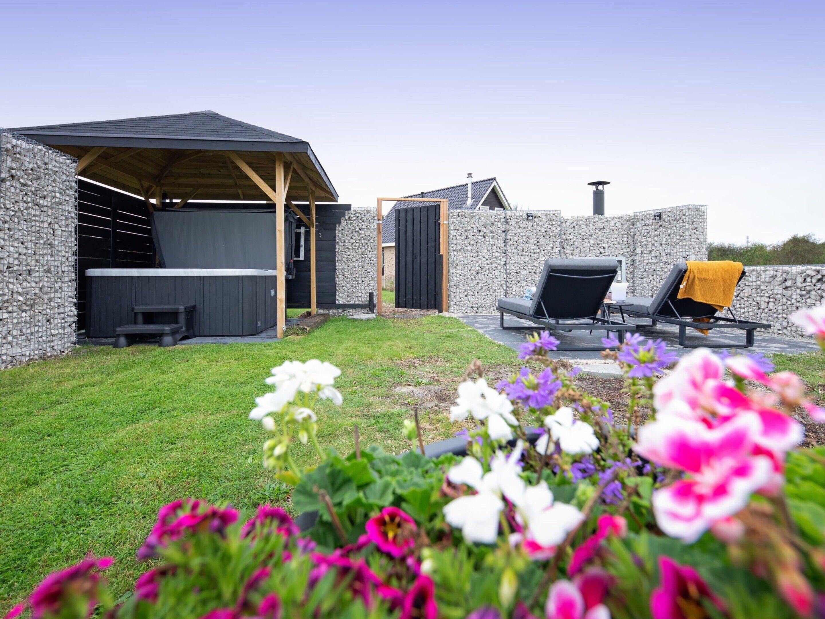 Una moderna area patio esterna con un muro in pietra, una pergola in legno e poltrone relax.
