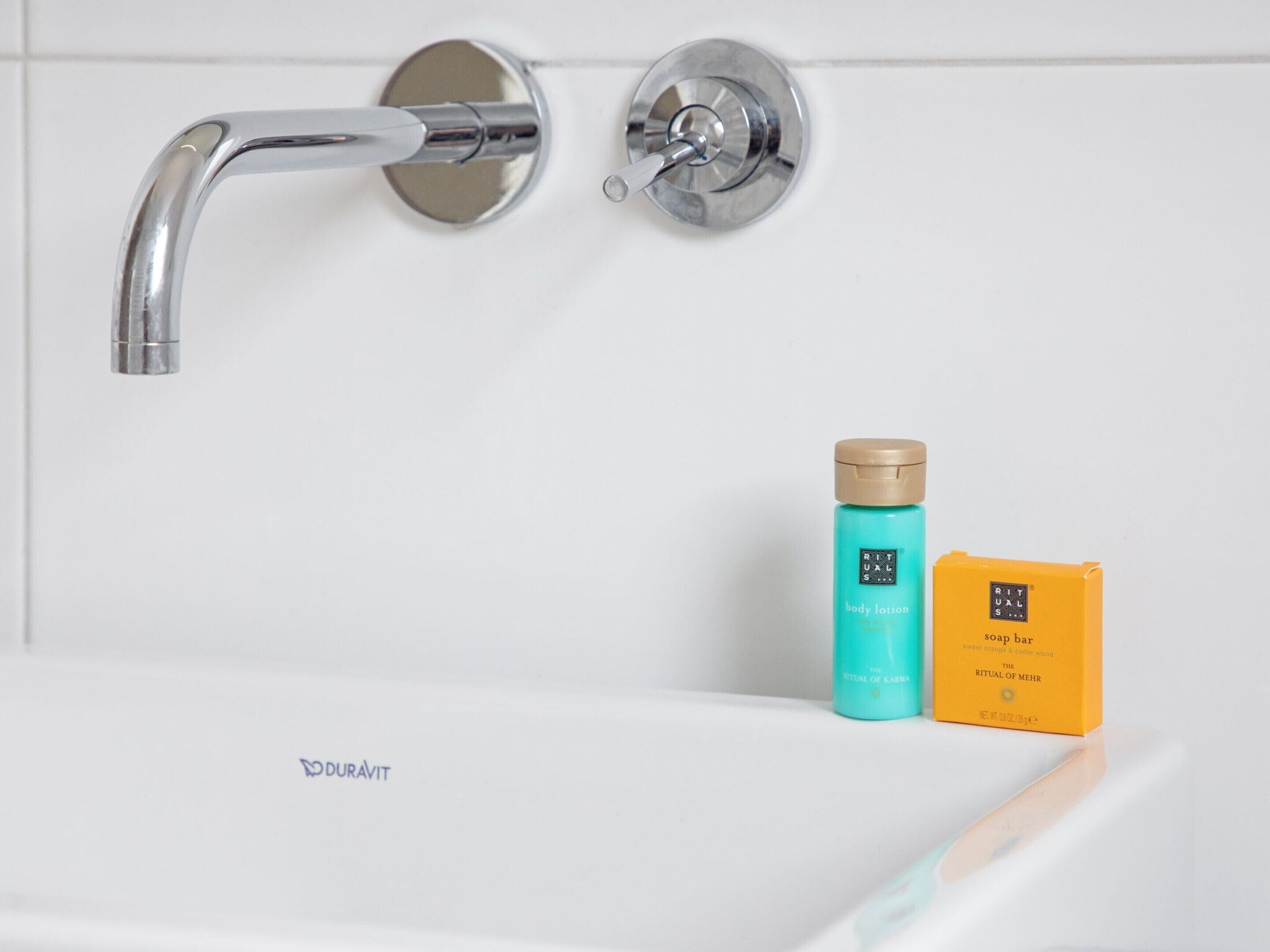Une salle de bain avec un lavabo blanc, un robinet chromé et deux flacons de lotion pour le corps et un savon.